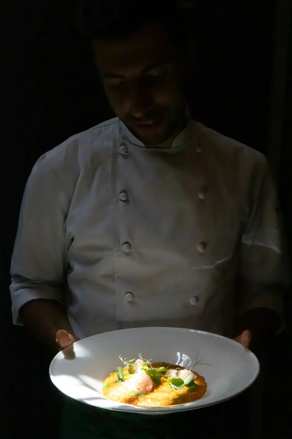 A chef holds a finished plate in a dark kitchen