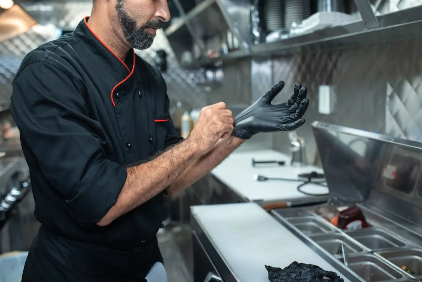 A cook puts on black gloves before prep